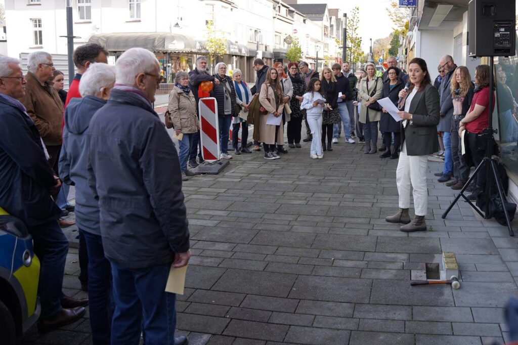 Menschenmenge auf einer Straße, Zuhörer hören einer Sprecherin zu.