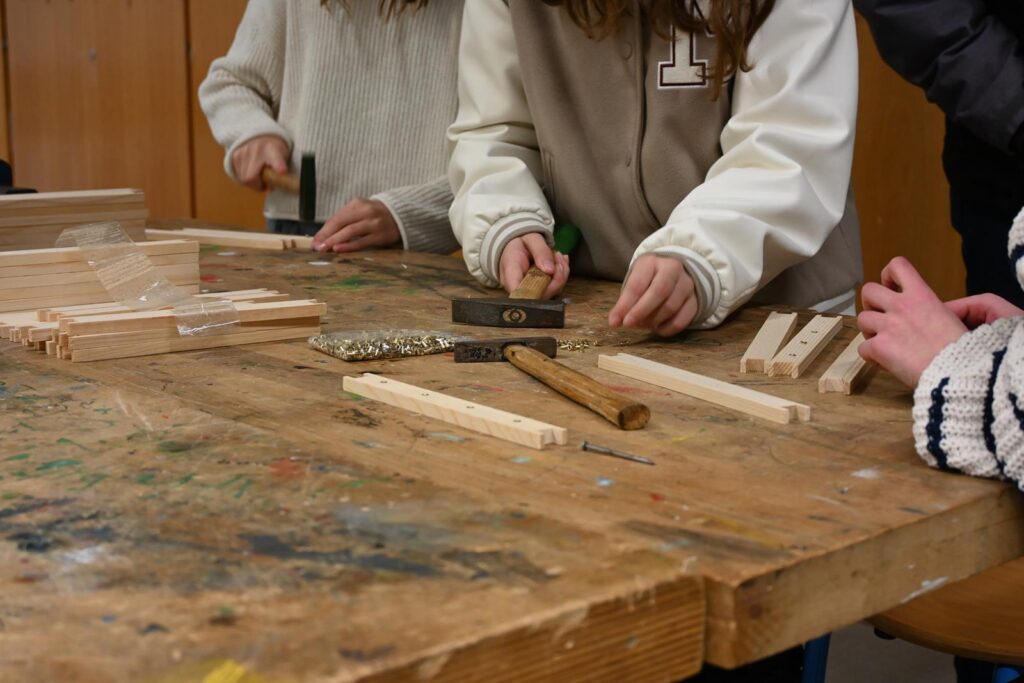 Schüler arbeiten an einem Werkstück mit Holz und Werkzeugen.