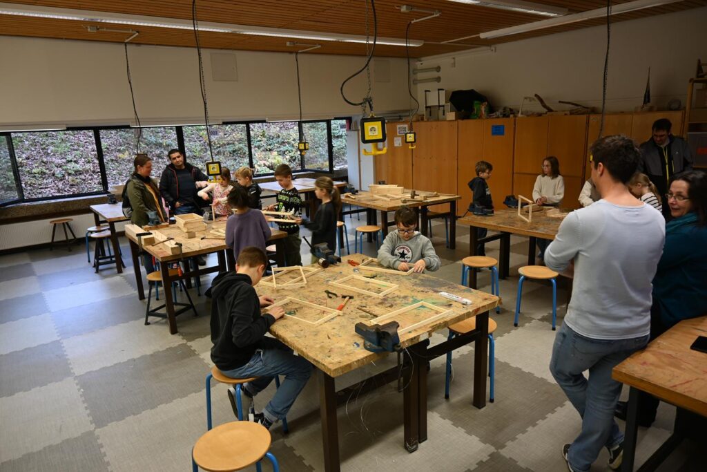 Schüler arbeiten an Holzbauten in einem Klassenzimmer mit vielen Tischen.
