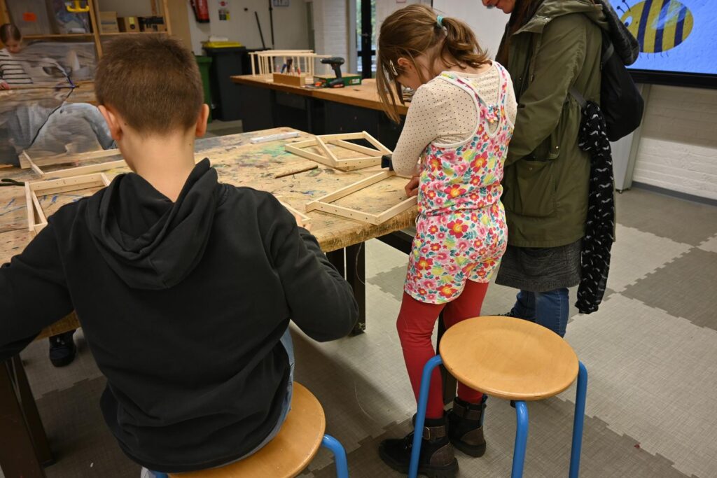 Kinder arbeiten an einem Tisch mit Holzrahmen in einem Klassenraum.