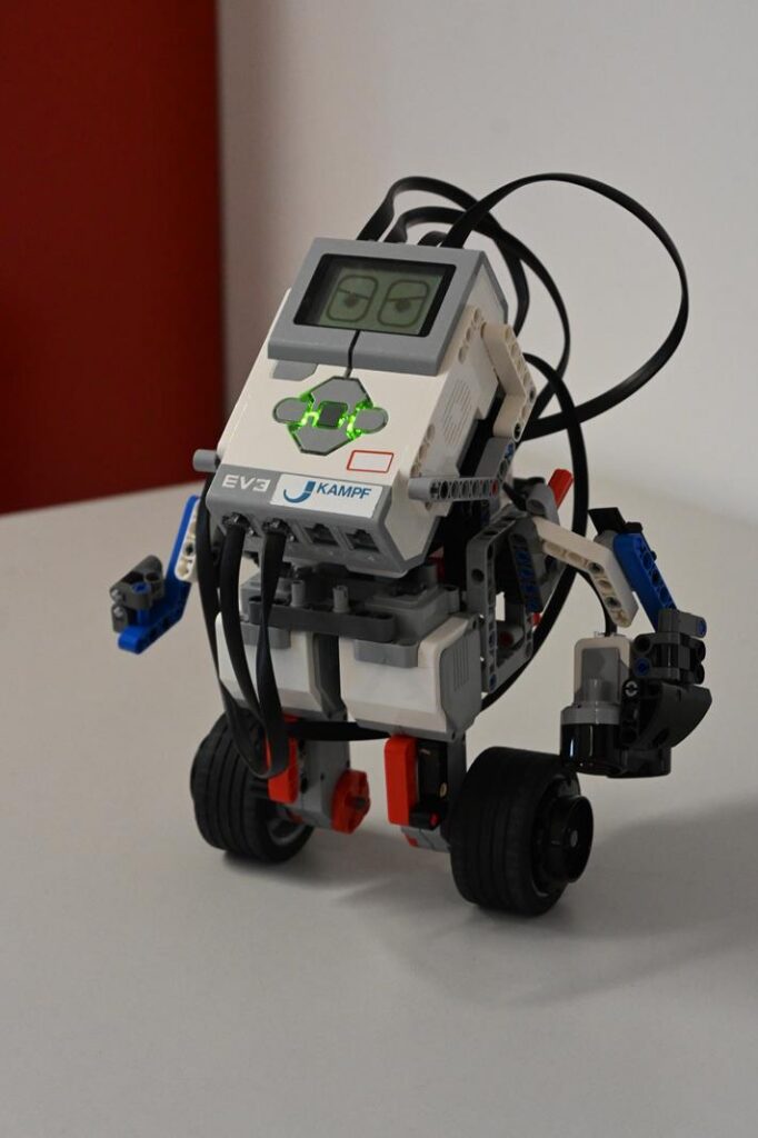 Ein kleiner Roboter steht auf einem Tisch mit digitalen Anzeigen.
