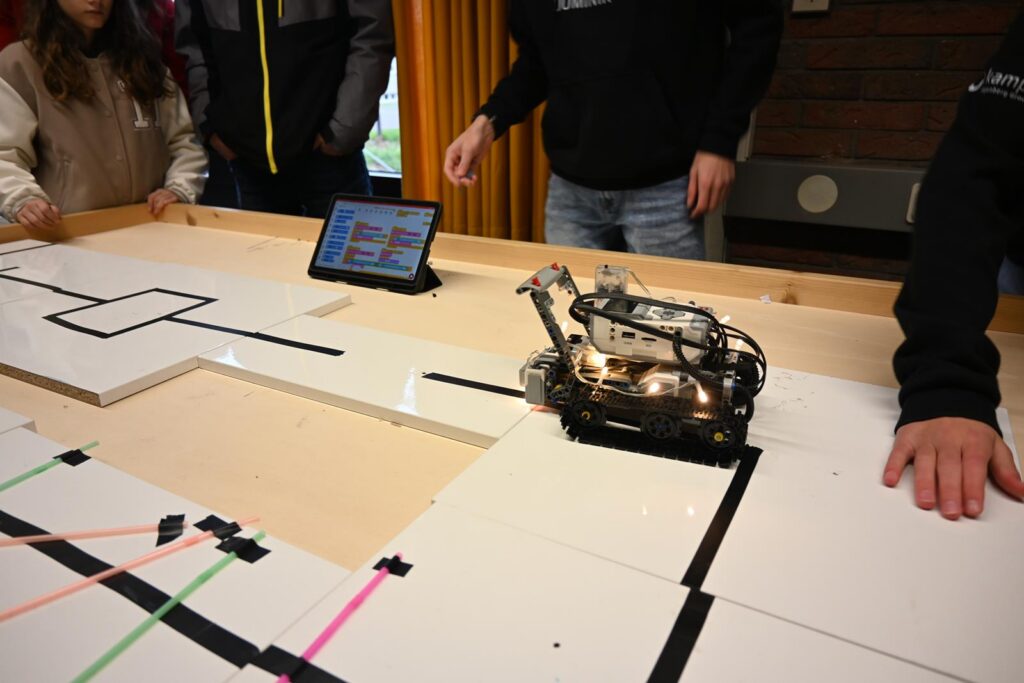 Ein Roboter navigiert auf einer Strecke, umgeben von Teilnehmern und einem Tablet.