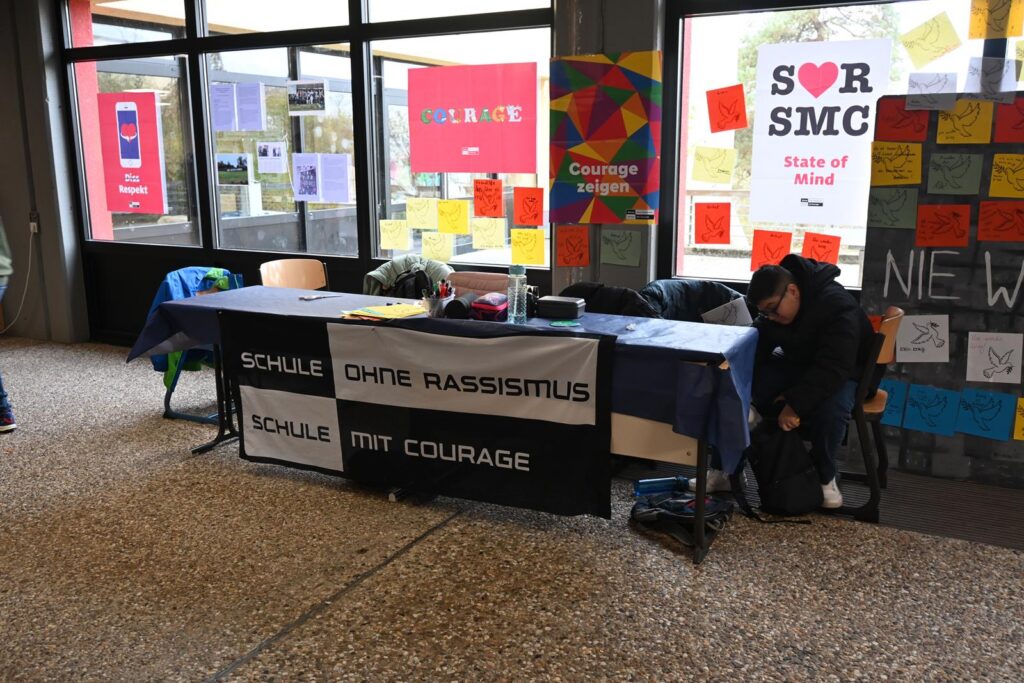 Tisch mit Banner "Schule ohne Rassismus, Schule mit Courage" in einem Raum.