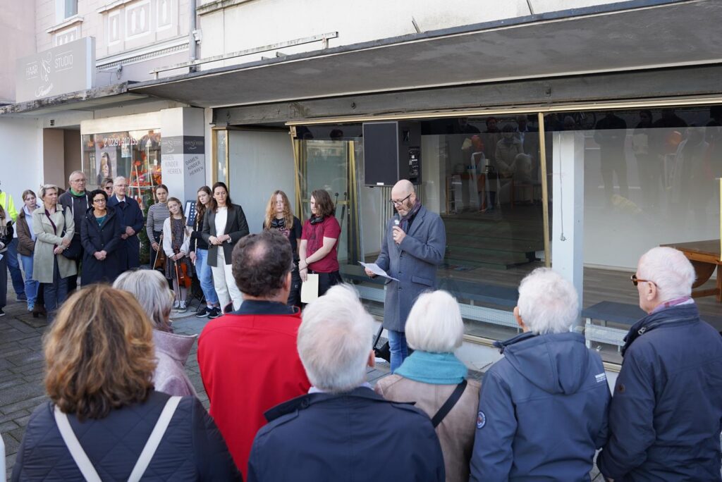 Menschen stehen vor einem Fenster, einige hören einem Redner zu.