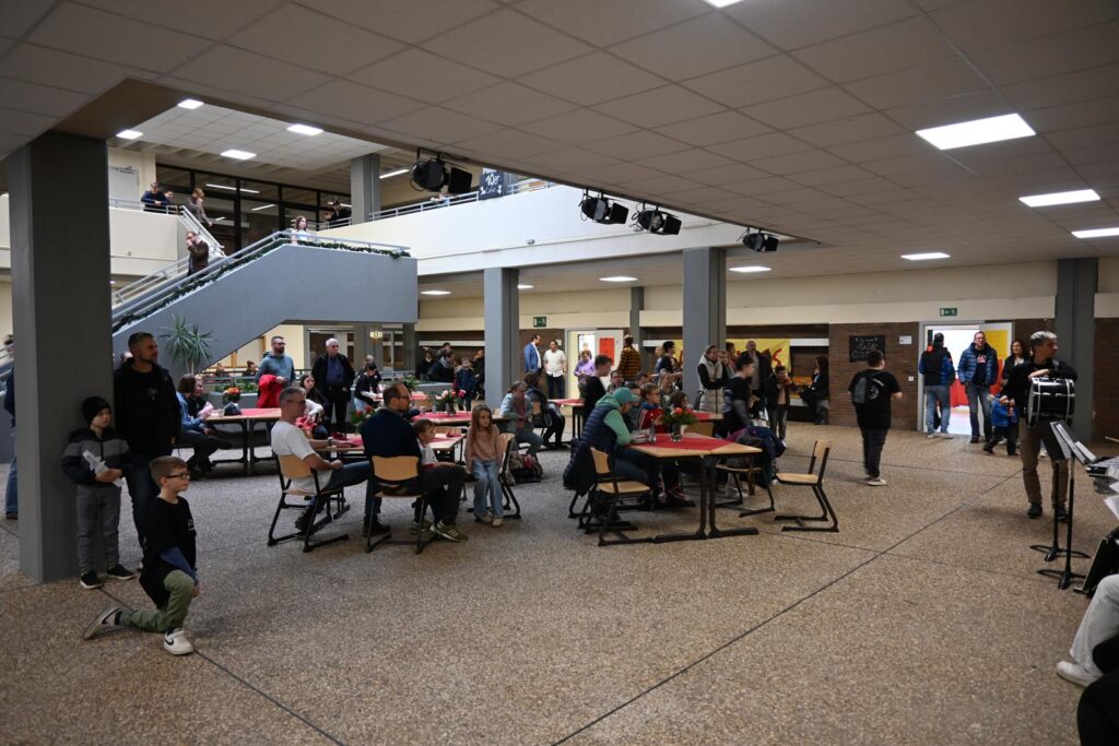 Schüler und Besucher in einem großen Atrium mit Tischen und einer Treppe.
