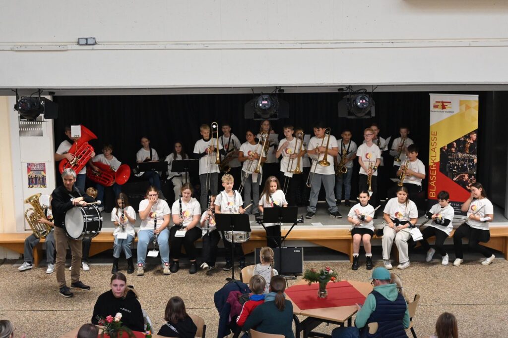 Schulband spielt auf der Bühne vor Publikum in einer Aula.