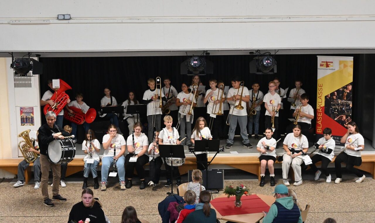 Schulband spielt auf der Bühne vor Publikum in einer Aula.