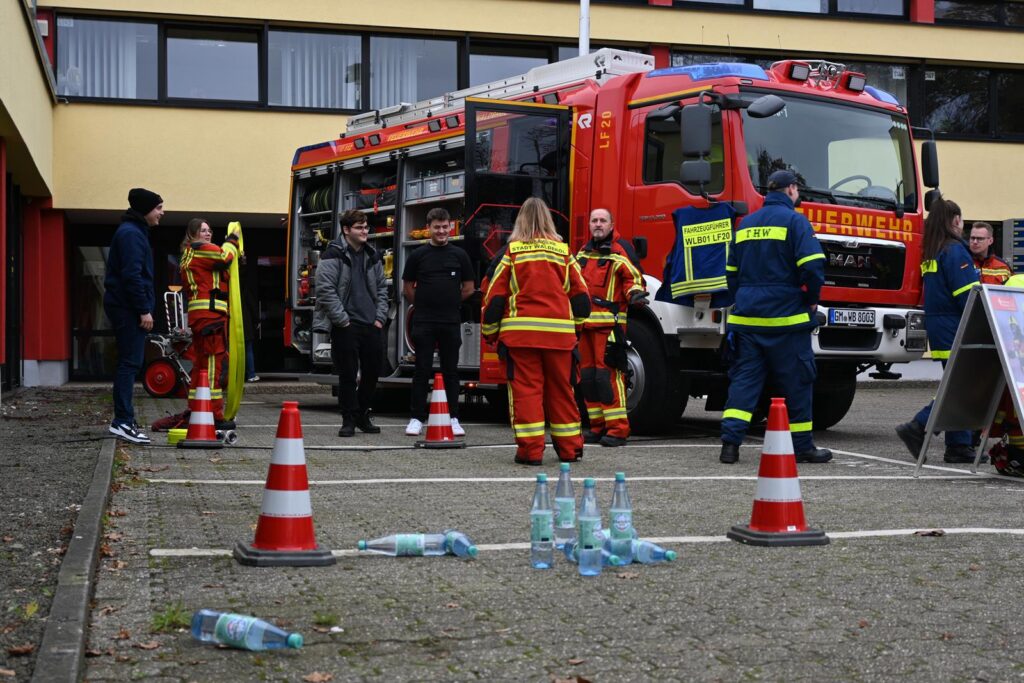 Feuerwehrfahrzeug mit Einsatzkräften, Menschen und Warnkegel auf dem Schulgelände.