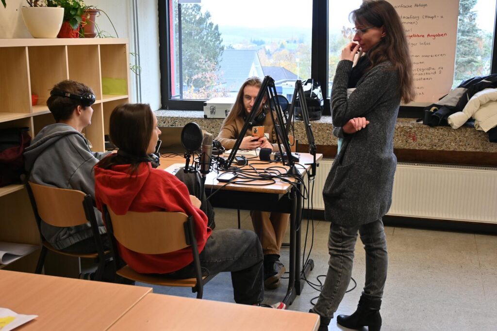 Schüler arbeiten an einem Tisch mit Mikrofonen und Technik in einem Klassenraum.