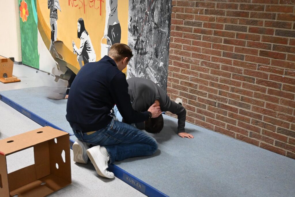 Zwei Schüler üben eine Körperübung an einer Wand mit Graffiti.
