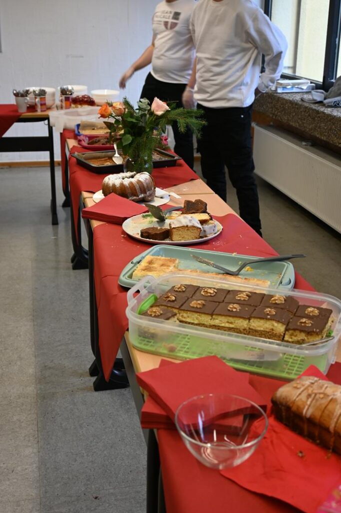 Tisch mit verschiedenen Kuchen und Süßigkeiten, dekoriert mit Blumen.