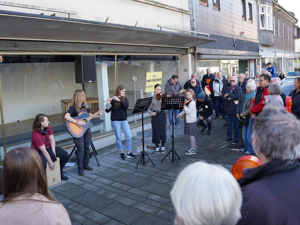 Musikgruppe spielt auf der Straße, Publikum schaut interessiert zu.