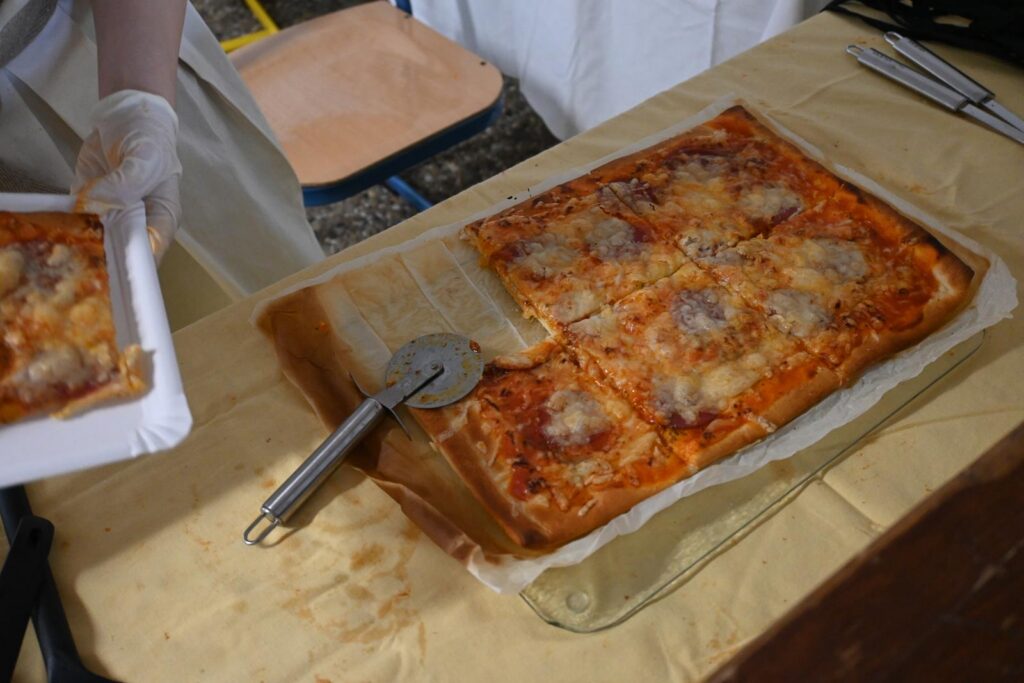 Auf einem Tisch liegt eine frisch gebackene Pizza mit Fleischstücken.