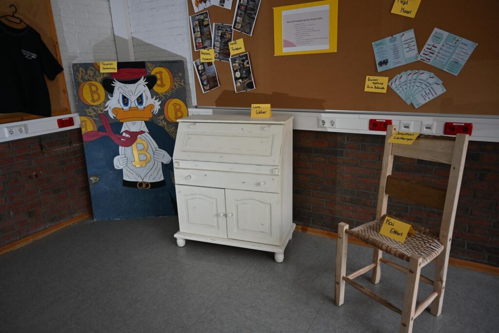 Ein weißes Schreibmöbel und ein Stuhl stehen in einem Klassenzimmer.