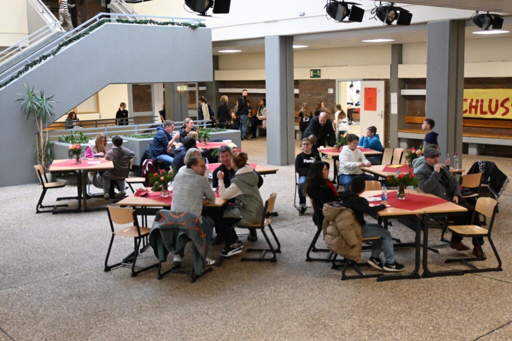 Schüler und Lehrer sitzen an Tischen in einer Schulcafeteria.