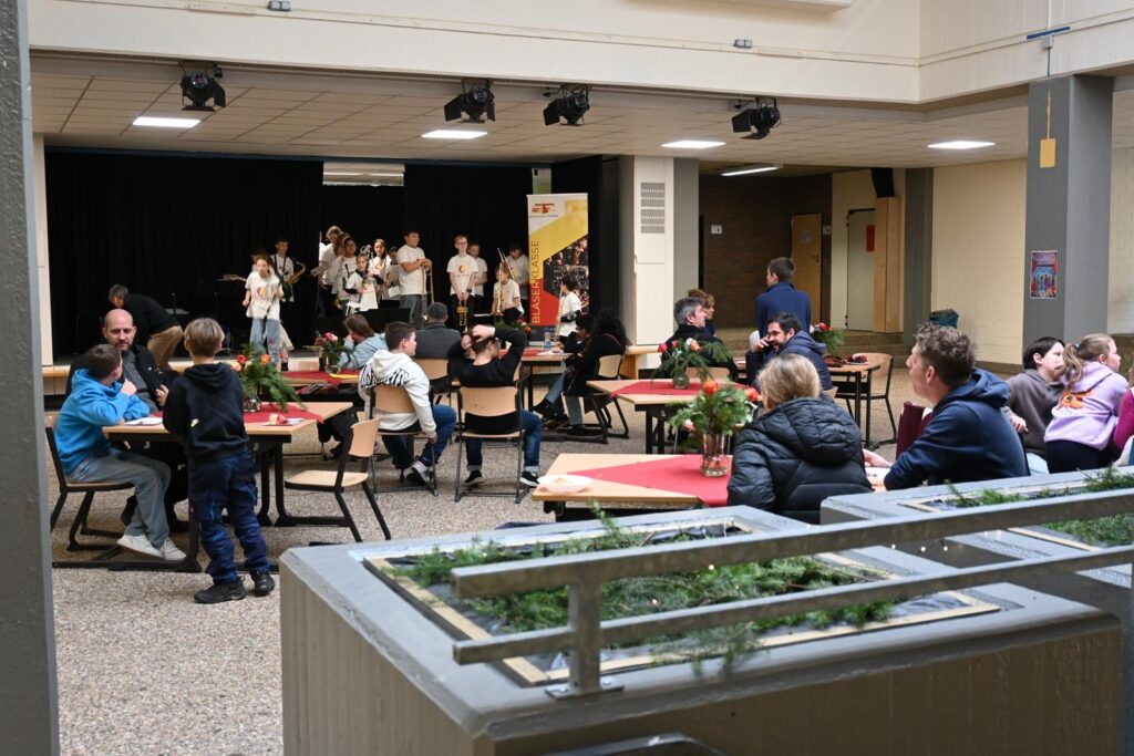 Veranstaltungssaal mit Menschen, Tischen und einer Band auf der Bühne.