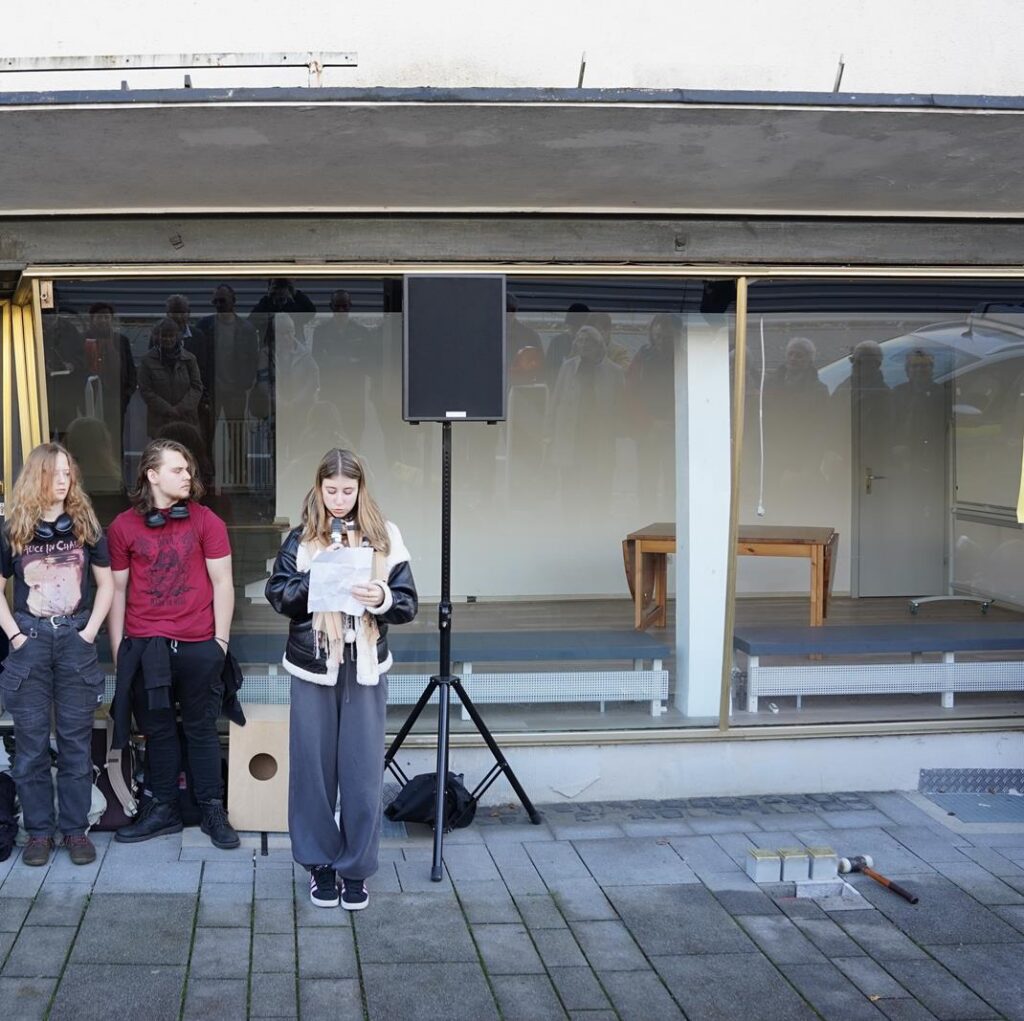 Gruppierung von drei Personen vor einem Fenster, darunter ein Lautsprecher.