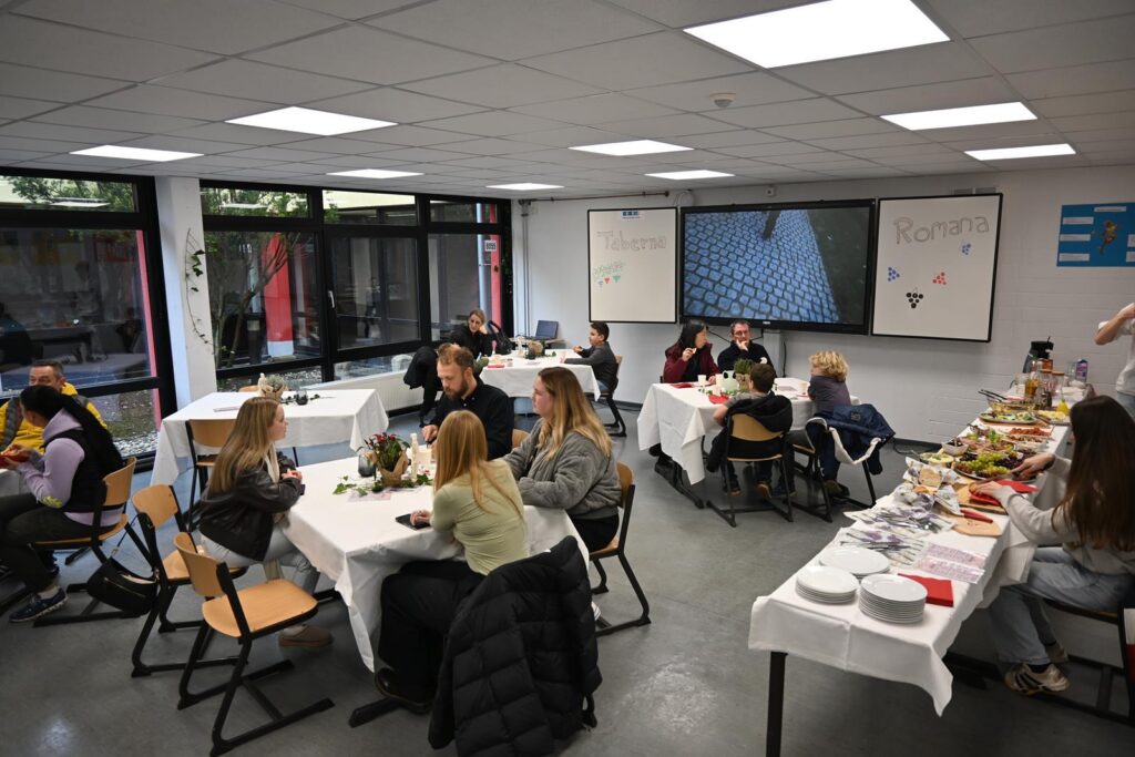 Schüler sitzen an Tischen in einem Raum, essen und unterhalten sich.
