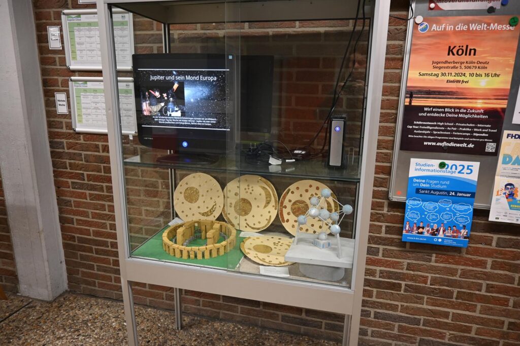 Vitrine mit verschiedenen Holzobjekten und einem Bildschirm.