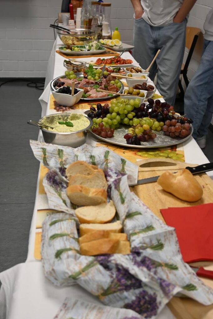 Buffet mit verschiedenen Speisen, Obst, Brot und Dips auf einem Tisch gedeckt.