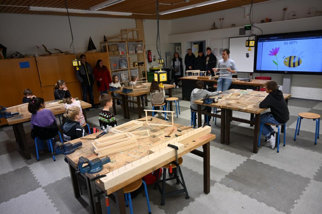 Schüler arbeiten in einer Werkstatt, ein Lehrer erklärt an der Tafel.