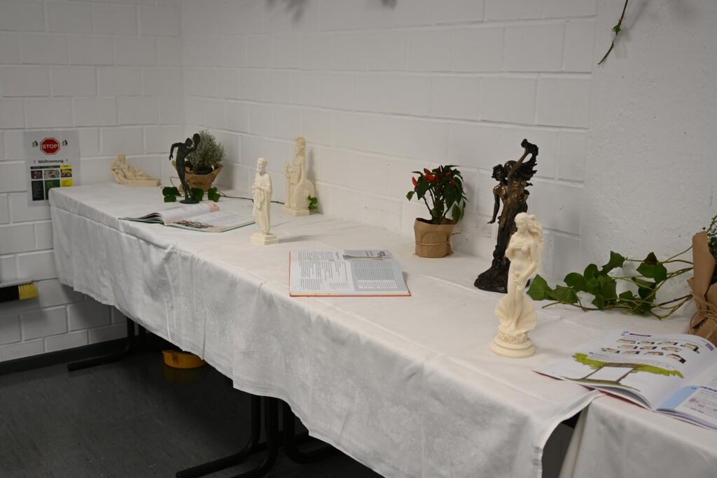 Tisch mit Statuen und Pflanzen vor einer weißen Wand.