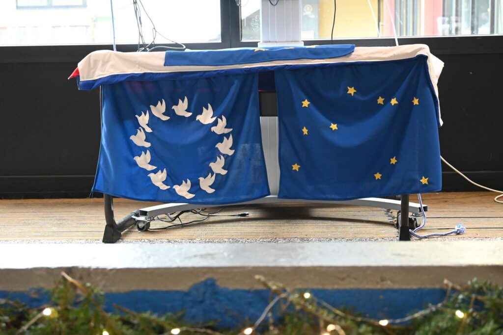 Blauer Tisch mit EU- und Friedenstauben-Flaggen. Dekoration im Hintergrund.