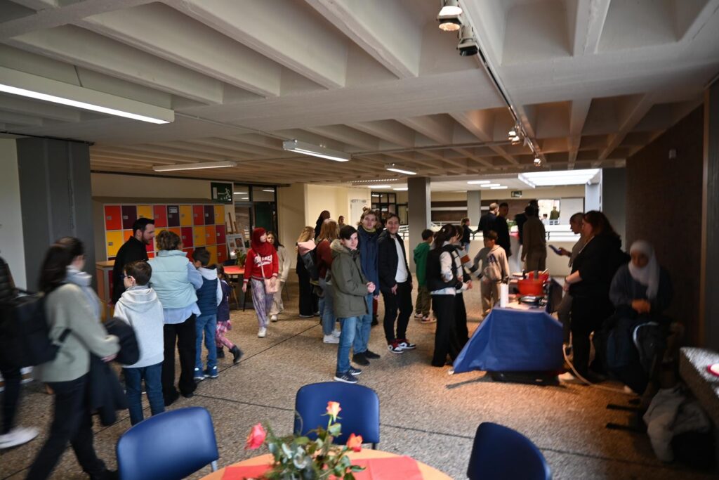 Schüler und Erwachsene in einem Raum bei einer Veranstaltung, Tische und Dekorationen sichtbar.