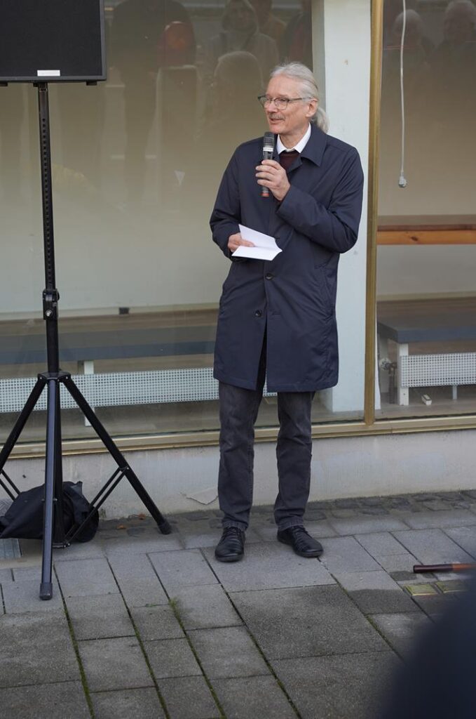 Mann steht mit Mikrofon und spricht vor einem Publikum.