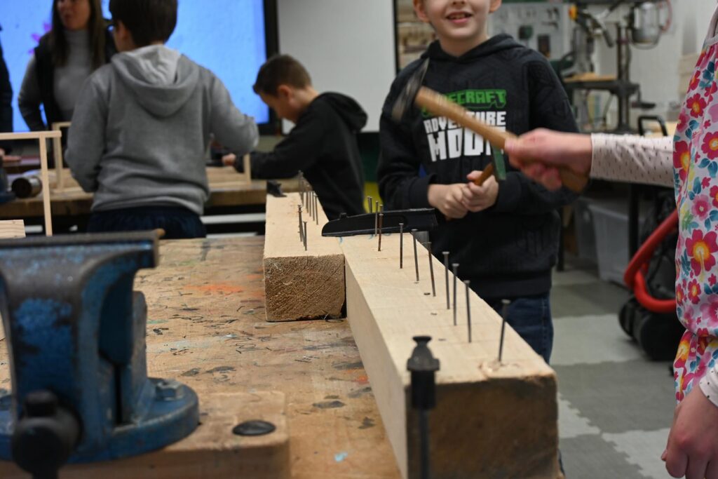 Schüler in Werkstatt beim Hämmern von Nägeln in ein Holzbrett.