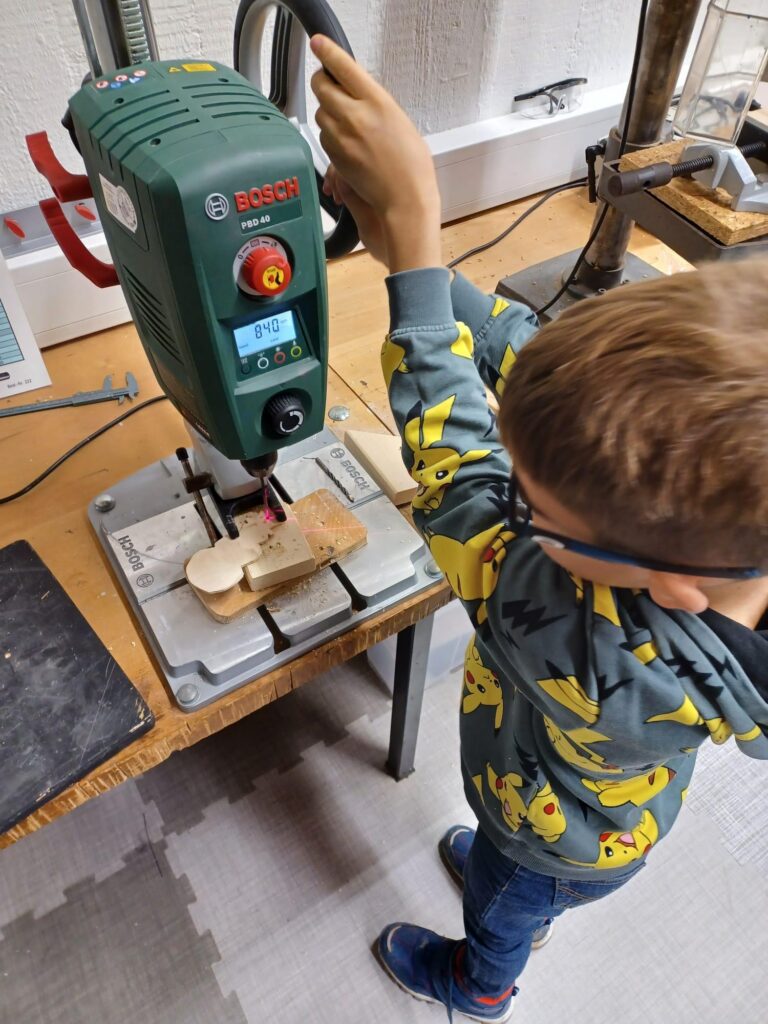 Kind arbeitet mit einer Bohrmaschine an einem Holzstück.