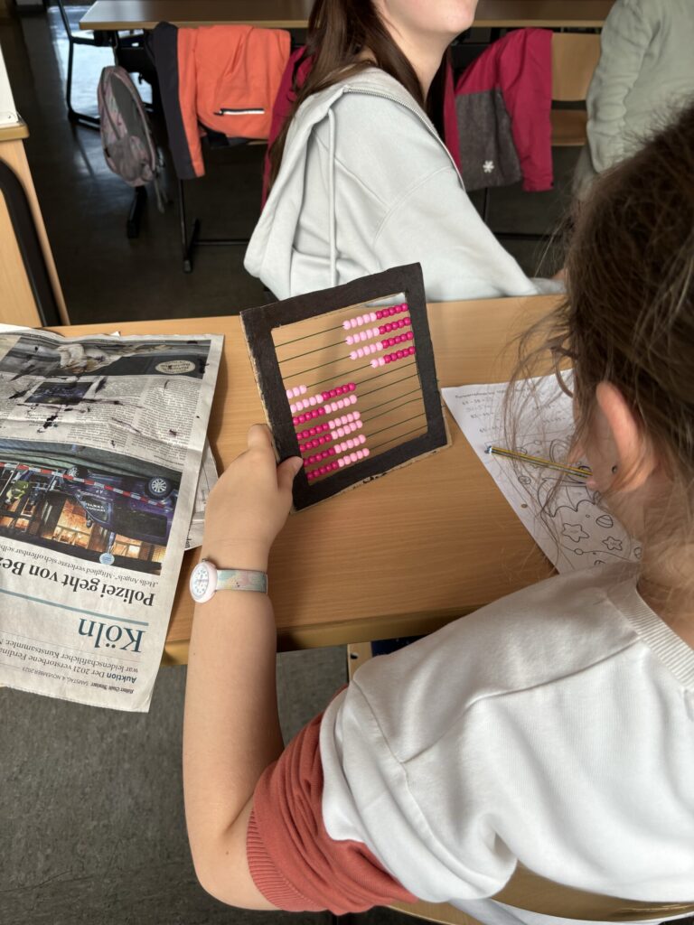 Schülerin hält ein Rechenmaterial und schaut auf ein Arbeitsblatt in der Klasse.