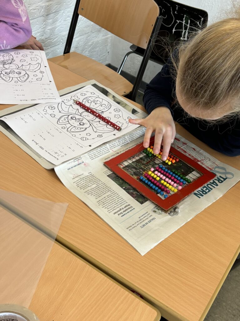 Ein Kind nutzt ein Rechengerät auf einem Tisch mit Ausmalbildern.
