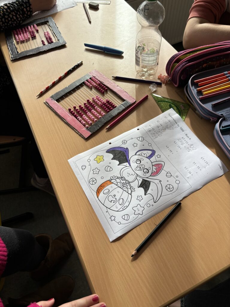 Kinder arbeiten an Mal- und Zeichenprojekten am Tisch. Farbstifte sind verteilt.
