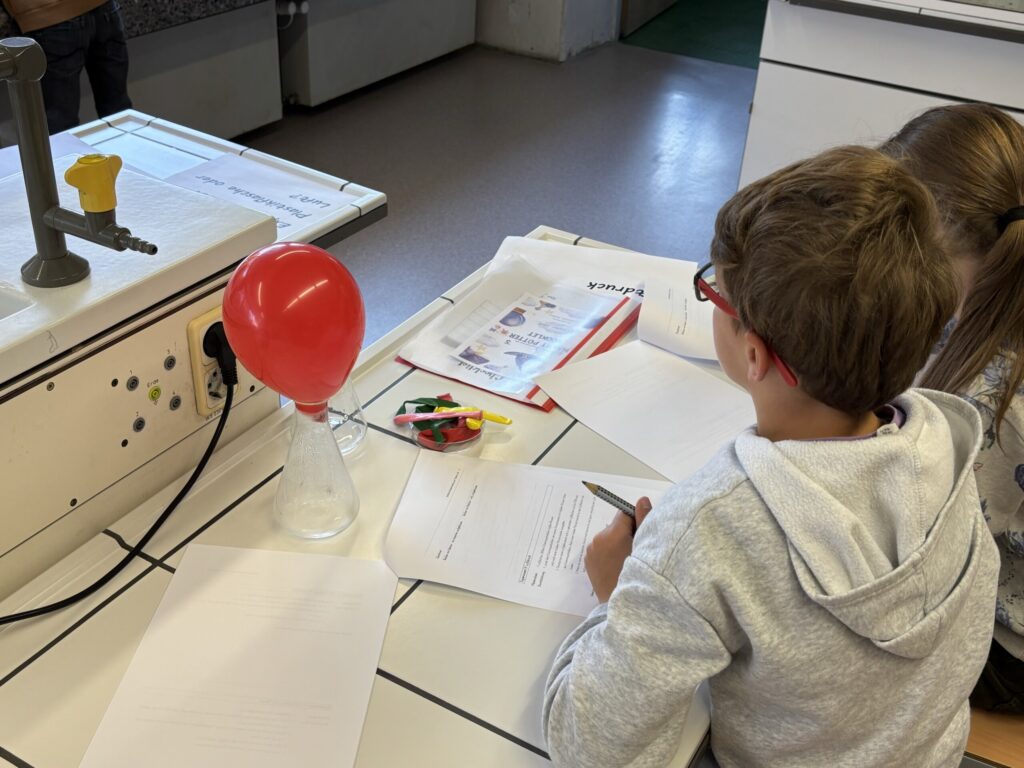 Zwei Schüler arbeiten an einem Experiment mit einem Ballon und einer Flasche.