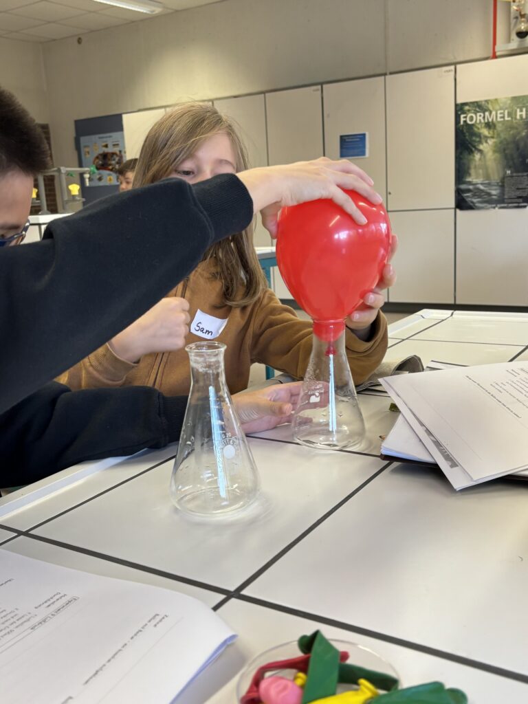 Schüler experimentieren mit einem roten Ballon und Erlenmeyerkolben im Chemielabor.