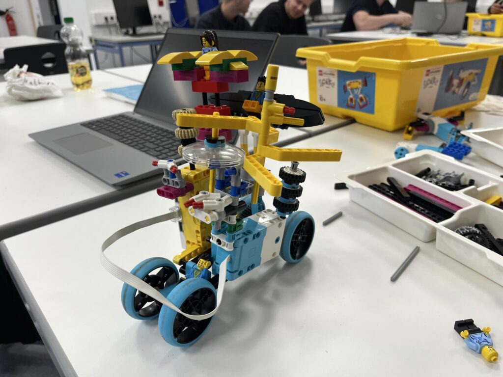 Buntes LEGO-Fahrzeug mit Rädern und einem Rotor auf einem Arbeitstisch.