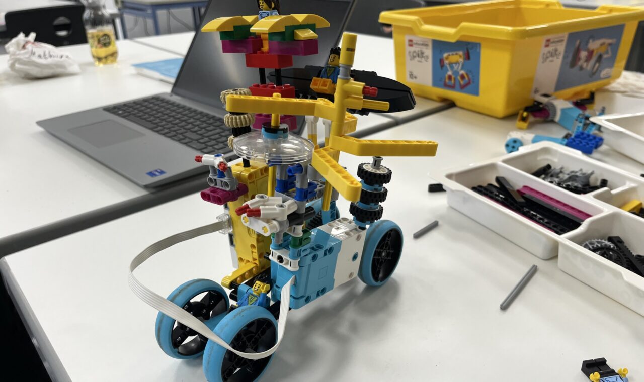Buntes LEGO-Fahrzeug mit Rädern und einem Rotor auf einem Arbeitstisch.