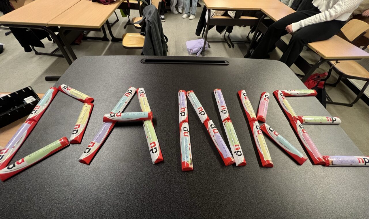 Auf einem Tisch liegt das Wort "DANKE", geschrieben aus bunten Schokoladenriegeln.