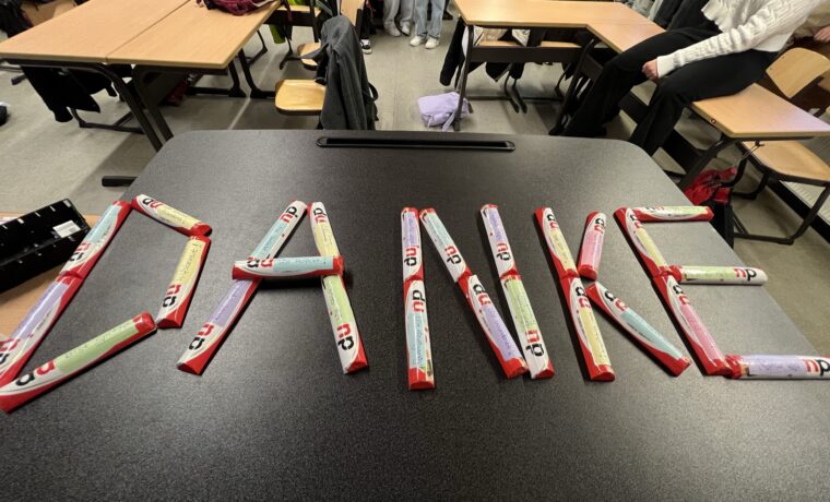 Auf einem Tisch liegt das Wort "DANKE", geschrieben aus bunten Schokoladenriegeln.
