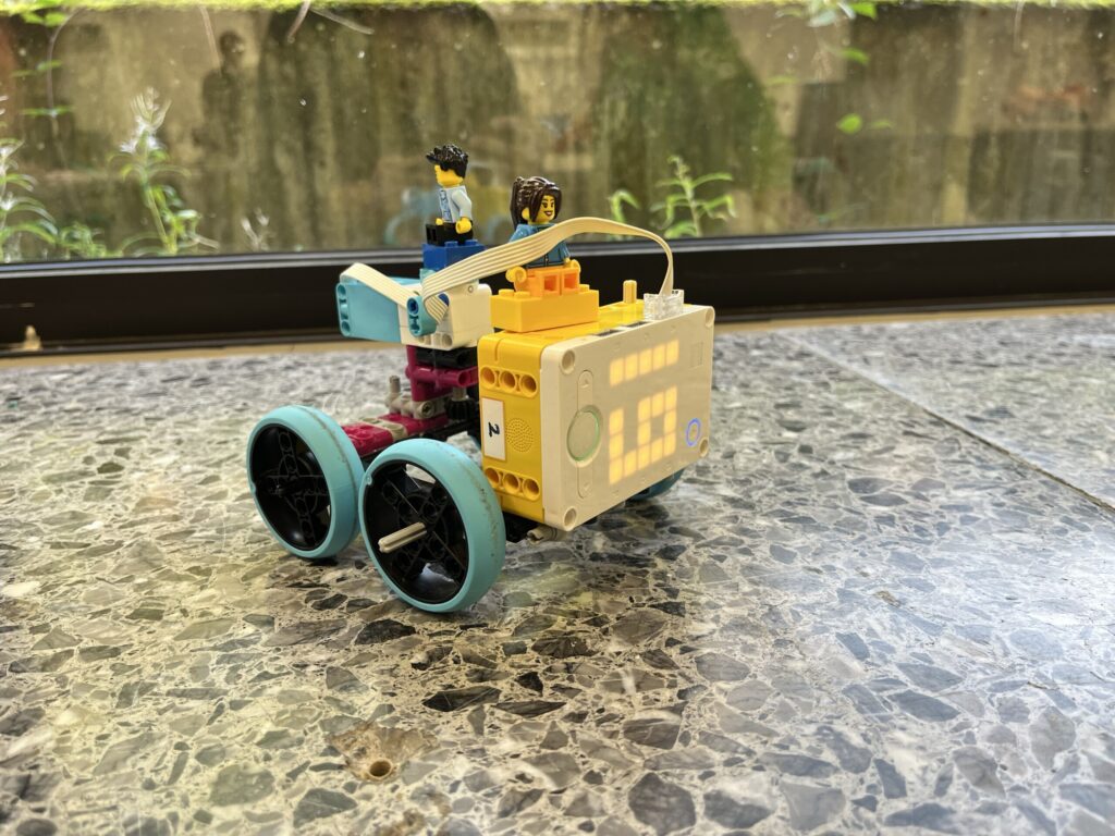 Ein bunter Roboterwagen mit zwei Figuren und großen Rädern auf einem Tisch.