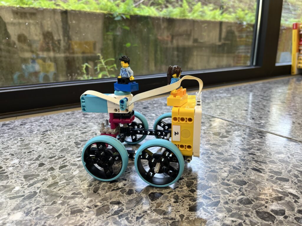Bunter LEGO-Roboter mit zwei Figuren auf einem Steinboden.