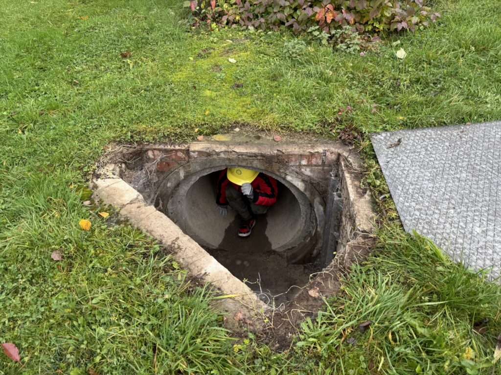 Ein Mensch mit Schutzhelm sitzt in einem Schacht im Boden.