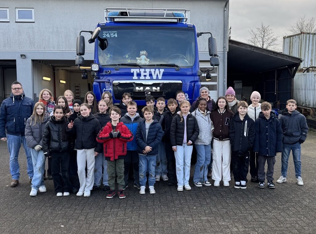 Gruppe von Schülern und Betreuern vor einem THW-Fahrzeug.