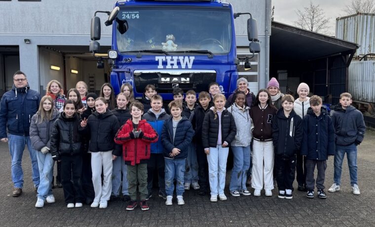 Gruppe von Schülern und Betreuern vor einem THW-Fahrzeug.