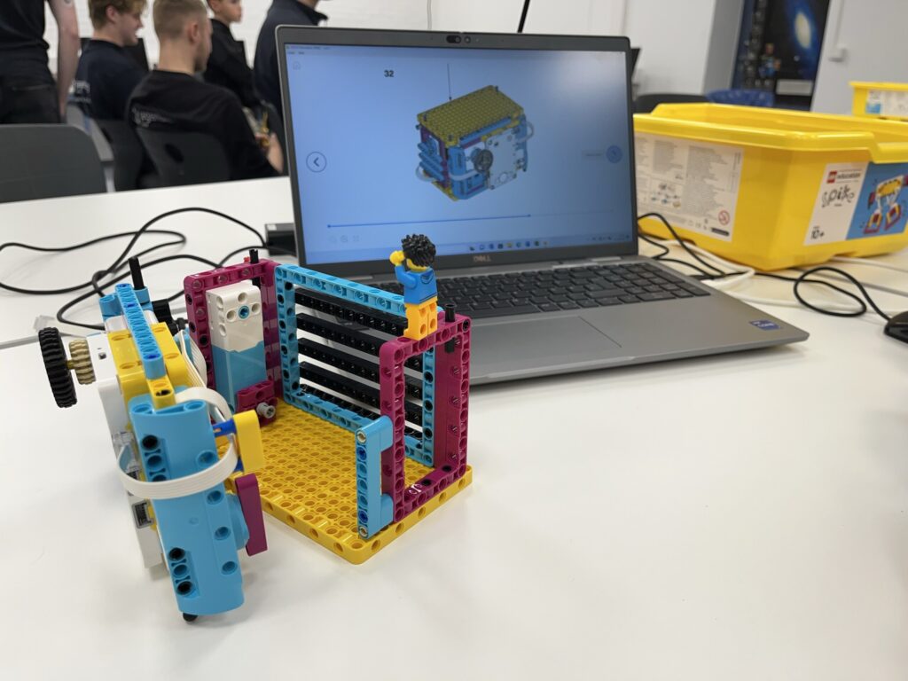 Buntes LEGO-Modell steht auf einem Tisch neben einem Laptop mit CAD-Darstellung.