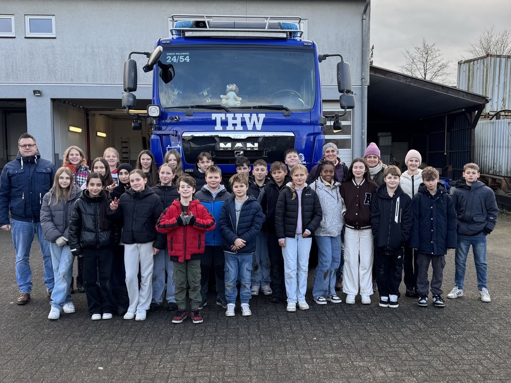 Gruppe von Schülern und Betreuern vor einem THW-Fahrzeug.