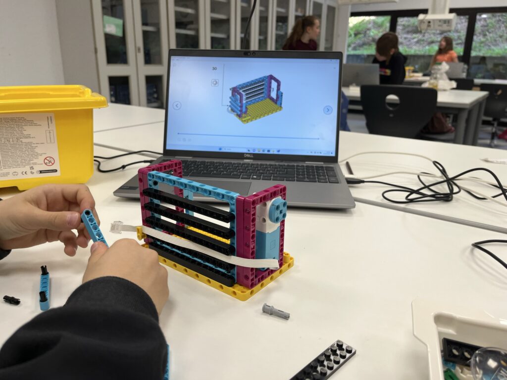 Ein Schüler baut mit LEGO Baukästen, während ein Bildschirm die Anleitung zeigt.