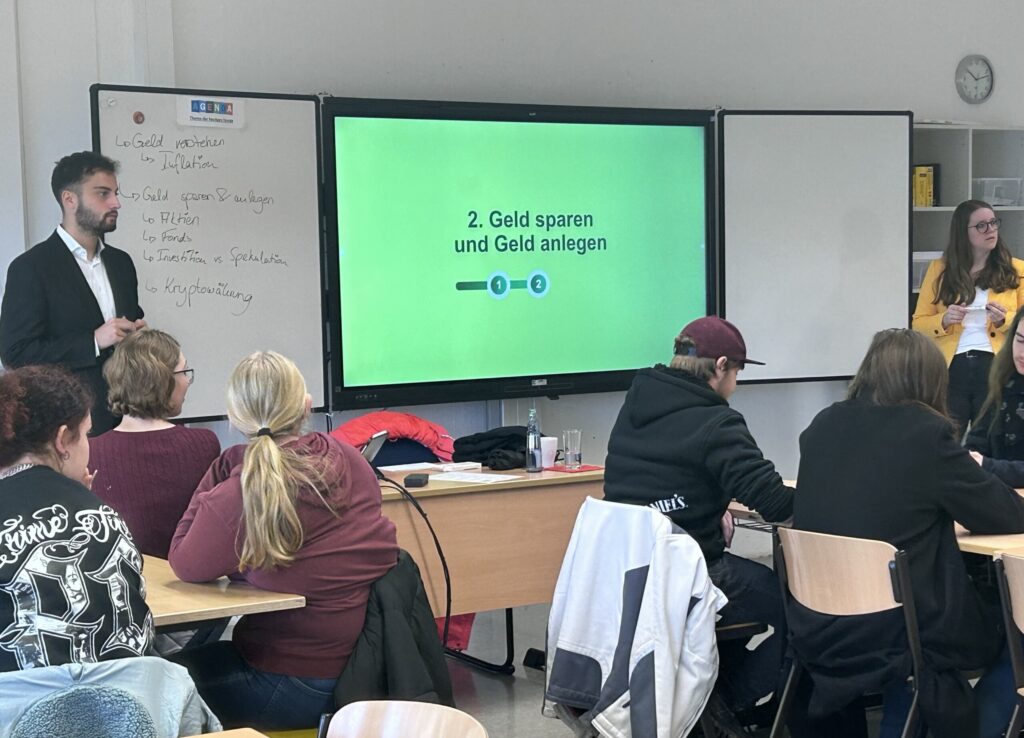 Lehrer erklärt Schülern das Thema Geld sparen und anlegen in einem Klassenraum.