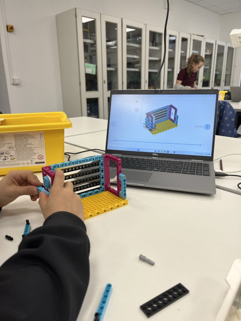 Schüler baut mit Legosteinen nach digitaler Anleitung an einem Tisch.